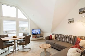 A modern living room with a sofa, a dining table, and a television. - Holiday apartment with 2 bedrooms (Wangerland Horumersiel)