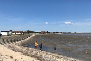 A beach with a clear sky, a sandy shore, and a few people walking along the water's edge. - Holiday apartment with 2 bedrooms (Wangerland Horumersiel)