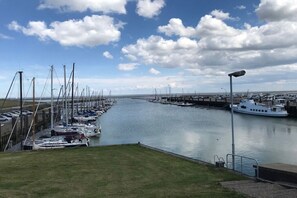 A marina with boats docked along a calm waterway, a grassy area in the foreground, and a clear sky. - Holiday apartment with 2 bedrooms (Wangerland Horumersiel)