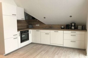 Een moderne keuken met witte kastjes, een inbouwoven, een koffiezetapparaat en een magnetron.