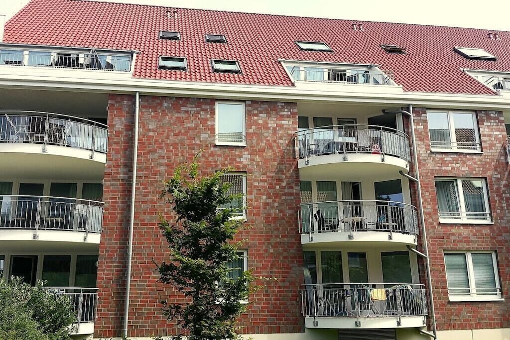 A multi-story residential building with balconies, brick facade, and red-tiled roof.