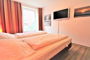 A hotel room with a bed, a television, and a window with curtains. - Residence Hohe Lith Type D (Cuxhaven-Duhnen)