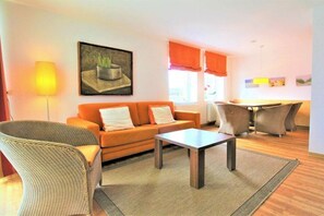 A living room with a sofa, a coffee table, and a dining area with chairs. - Residence Hohe Lith Type D (Cuxhaven-Duhnen)