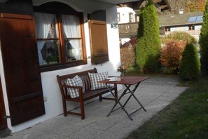 A wooden bench with checkered cushions, a small table, and a window with curtains. - Am Sonneneck - Apartment 1 (Ruhpolding)