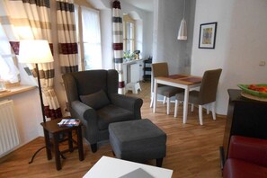 A living room with a sofa, ottoman, dining table, chairs, and a lamp. - Am Sonneneck - Apartment 1 (Ruhpolding)