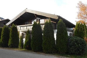 A traditional chalet-style building with a sloped roof, wooden balconies, and a well-maintained garden with coniferous trees. - Am Sonneneck - Apartment 1 (Ruhpolding)