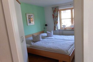 A room with a bed, a lamp, a window with curtains, and a framed picture on the wall. - Am Sonneneck - Apartment 1 (Ruhpolding)