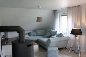 A modern living room with a sofa, a lamp, and a wood-burning stove. - Holiday apartment with 1 bedroom (Butjadingen - Tossens)