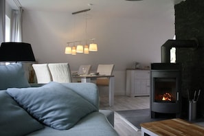A modern living room with a sofa, a dining table with chairs, a fireplace, and pendant lights. - Holiday apartment with 1 bedroom (Butjadingen - Tossens)