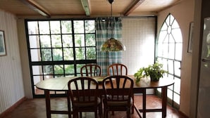 A dining area with a round table, four wooden chairs, a hanging pendant light, and a potted plant. - Holiday home with 3 bedrooms (Cabanas de Tavira)