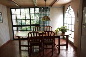 Ein Essbereich mit einem runden Tisch, vier Holzstühlen, einer hängenden Pendelleuchte und einem Topfpflanzen.