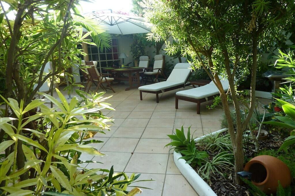 Un espace patio aménagé avec une table et des chaises, entouré de plantes et d’arbres.
