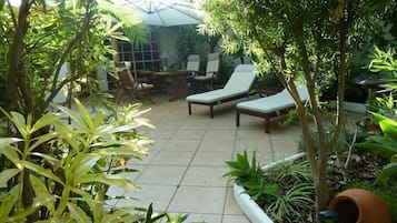 Área de pátio com mesa e cadeiras, cercada por plantas e árvores.