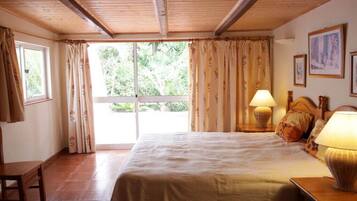 Quarto com cama, duas luminárias laterais, cabeceira de madeira, janela com cortinas e uma porta.