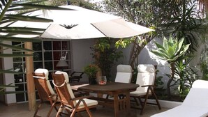 An outdoor patio with a round wooden table, four chairs, and a large umbrella providing shade. - Holiday home with 3 bedrooms (Cabanas de Tavira)