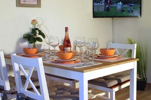 Een eettafel gedekt met oranje kommen, wijnglazen en een fles, met stoelen en een televisie op de achtergrond.