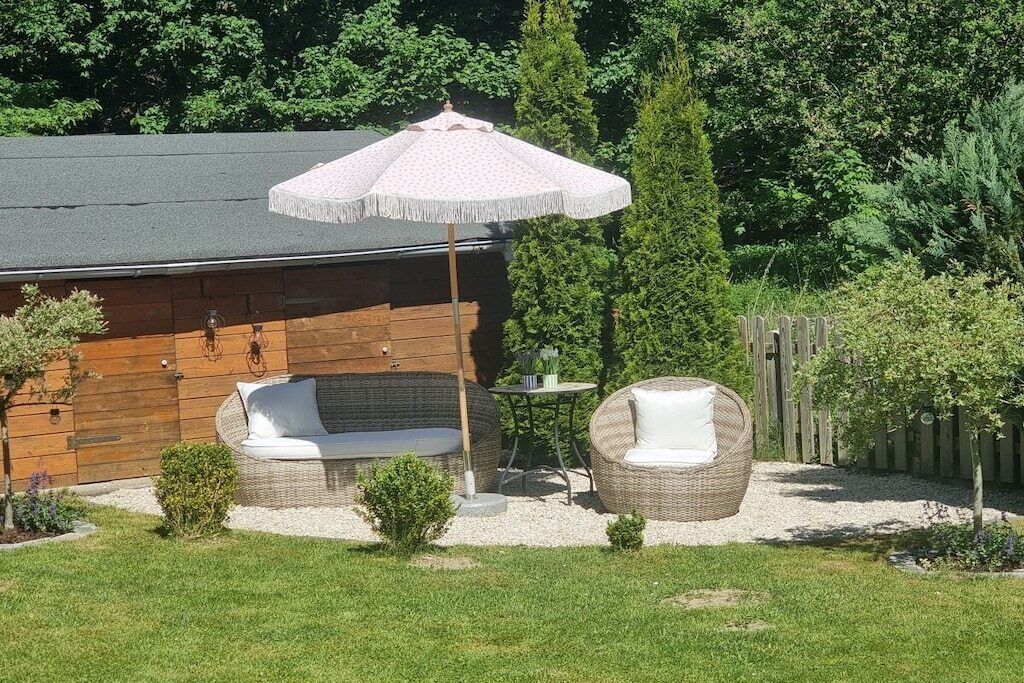 Eine Holzhütte mit zwei Korbstühlen und einem kleinen Tisch, umgeben von einer Schotterfläche und viel Grün.