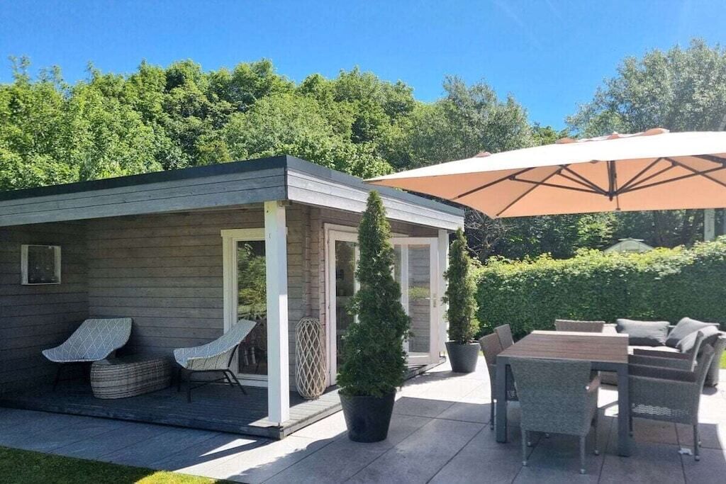 A covered outdoor seating area with a table and chairs, a small covered structure with a door, and potted plants.