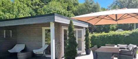 A covered outdoor seating area with a table and chairs, a small covered structure with a door, and potted plants.