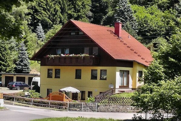 A two-story building with a red roof, a balcony with flower boxes, and a small outdoor seating area. - Holiday apartment with 1 bedroom (Bad Schandau Stadtteil Prossen)
