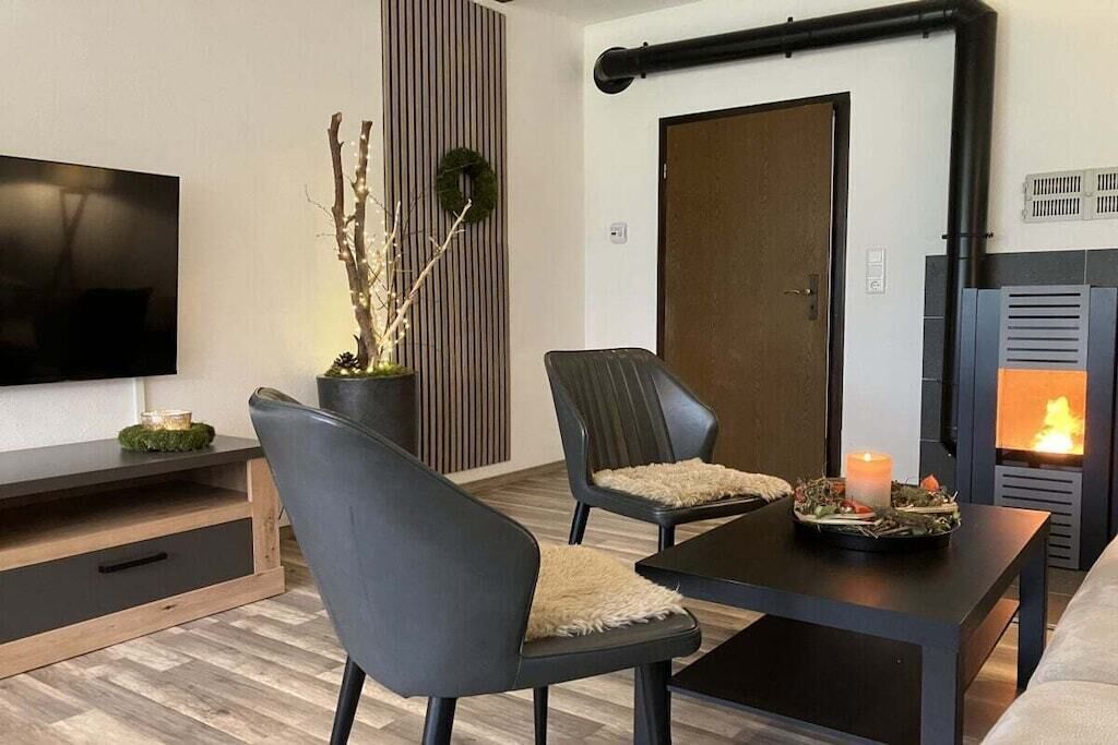 A modern living room with a flat-screen TV, two chairs, a small table with a candle, and a fireplace.