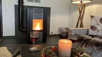 A cozy living room with a fireplace, a candle, and a glass of red wine on a table.