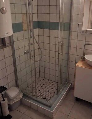 En dusch med en glasdörr, en toalett och ett handfat i ett badrum med kaklade väggar.