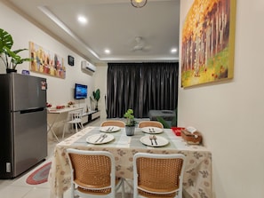 Comedor con una mesa preparada para cuatro personas, rodeada de sillas de mimbre, un refrigerador y un televisor de pantalla plana montado en la pared.