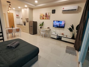 Habitación de hotel con cama, escritorio, televisor, refrigerador y comedor con sillas y mesa.