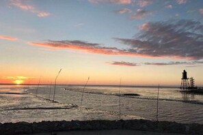 A coastal sunset with a lighthouse and calm sea. - Comfortable holiday home Mellumplate 32 (Wurster Nordseeküste (Ortsteil Dorum-Neufeld))