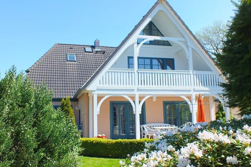 Et toetagers hus med en balkon, en blomsterprydet have og en klar himmel.