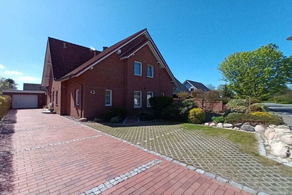 A two-story brick house with a sloped roof, a paved driveway, and a well-maintained front yard with a lawn and shrubs.