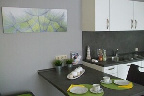 A modern kitchen with white cabinets, a black countertop, and a dining area with a table set for two. - Kerstin Rehm holiday apartment (Cuxhaven)