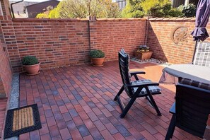 A patio with a brick floor, a black folding chair, a table, and potted plants. - Kerstin Rehm holiday apartment (Cuxhaven)