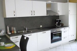 A modern kitchen with white cabinets, a black countertop, a coffee maker, and a sink. - Kerstin Rehm holiday apartment (Cuxhaven)