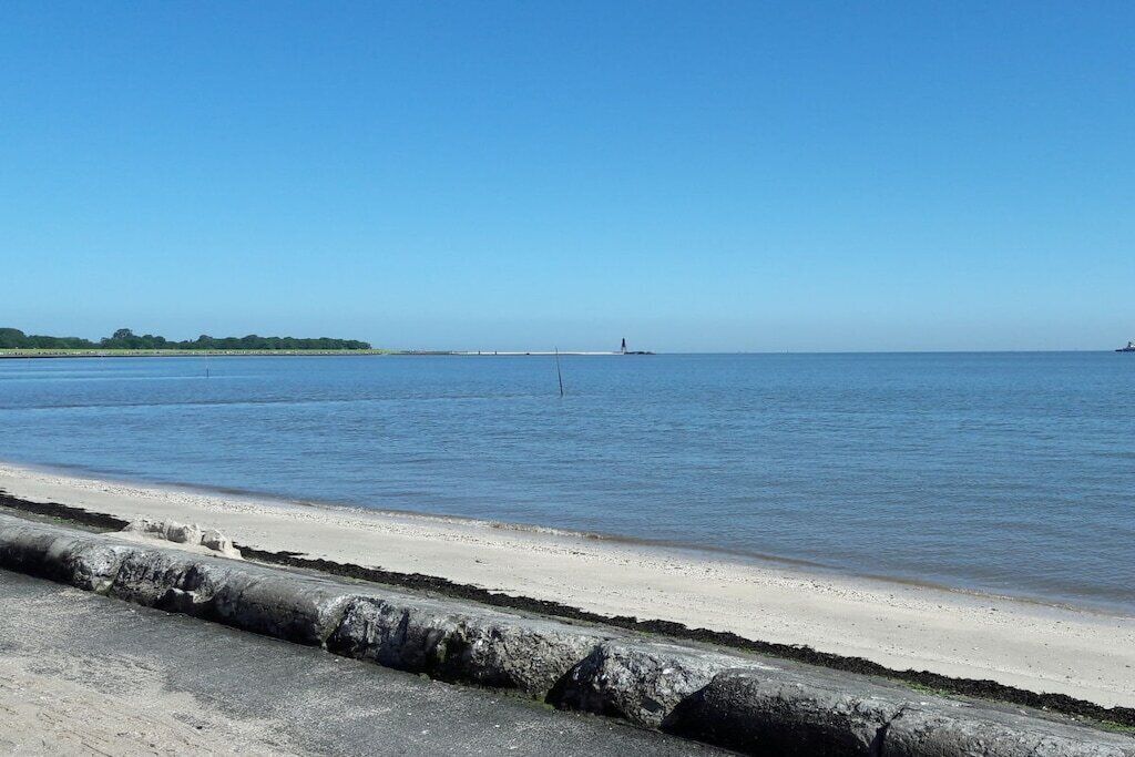 A coastal beach with a clear sky, calm water, and a distant lighthouse.