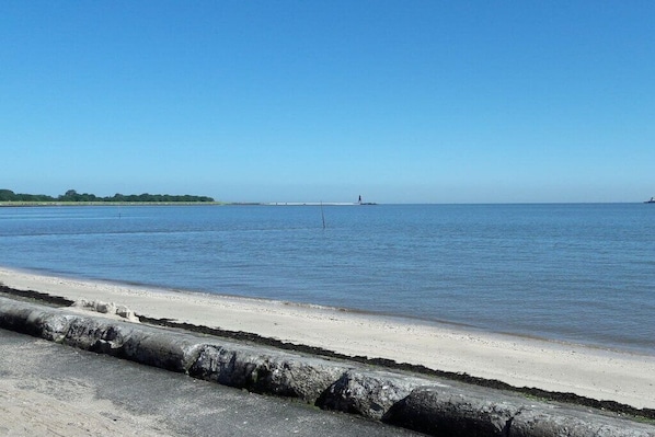 A coastal beach with a clear sky, calm water, and a distant lighthouse. - Kerstin Rehm holiday apartment (Cuxhaven)