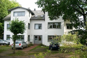 A two-story residential building with a white exterior, multiple windows, and a small front yard with two cars parked. - Holiday apartment Zaunkönig (Ostseebad Zinnowitz)