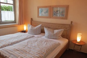A double bed with striped bedding and two pillows, a bedside table with a lamp, and two framed pictures on the wall. - Holiday apartment Zaunkönig (Ostseebad Zinnowitz)