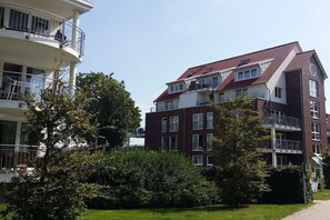 Een meerlaags woongebouw met balkons, een dak met rode tegels en een verzorgd gazon.
