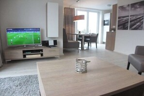 Ein modernes Wohnzimmer mit Fernseher, Couchtisch und Essbereich mit Tisch und Stühlen.