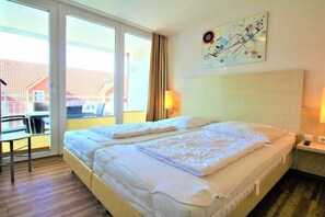 Een hotelkamer met twee bedden, een raam met gordijnen, een tafel en een kunstwerk aan de muur.