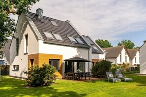 A modern two-story house with a sloped roof, a patio with a table and chairs, and a lawn with two sun loungers. - Schlehe, homestead by the Baltic Sea forest (Zingst)