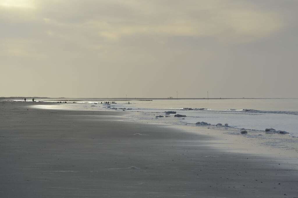 A beach with a pier extending into the water, a clear sky, and a calm sea.