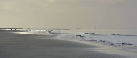 A beach with a pier extending into the water, a clear sky, and a calm sea.
