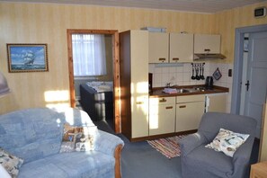 A compact living space with a kitchenette, two armchairs, a dining table, and a painting on the wall. - Holiday greetings in the house (Norddorf)