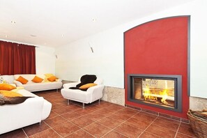 Een moderne woonkamer met een open haard, witte banken en oranje kussens.
