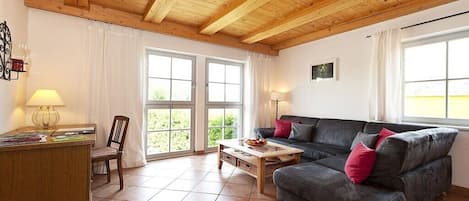 A living room with a wooden ceiling, a sofa, a coffee table, and a desk with a lamp.