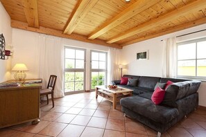 A living room with a wooden ceiling, a sofa, a coffee table, and a desk with a lamp. - Holiday apartment with 1 bedroom (Gohrisch OT Papstdorf)