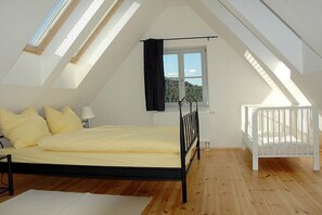A bedroom with a sloped ceiling, a bed, a crib, a window, and a radiator. - Holiday apartment with 1 bedroom (Gohrisch OT Papstdorf)